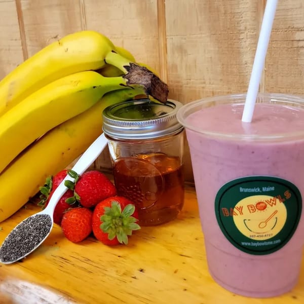 Bay Bowls smoothie with bananas, strawberries, honey, and chia seeds on a wooden surface.