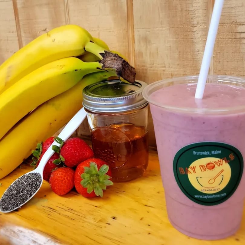 Bay Bowls smoothie with bananas, strawberries, honey, and chia seeds on a wooden surface.