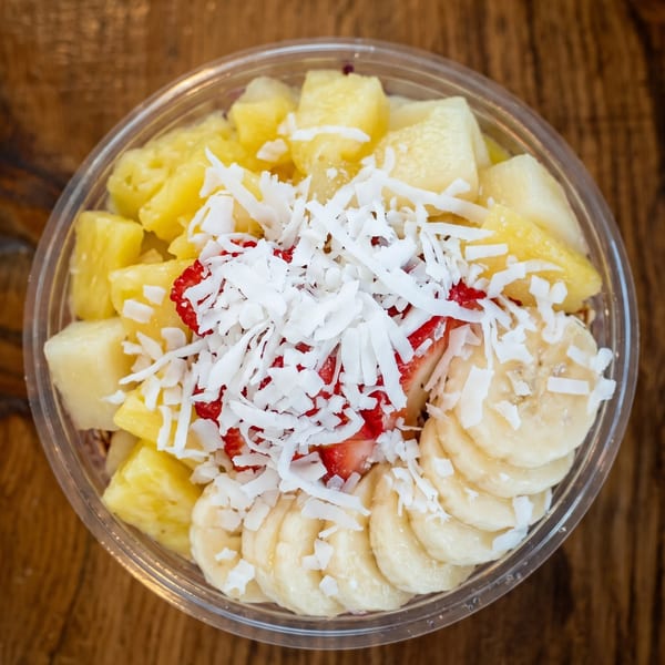 Overhead view of a fruit bowl with pineapple, strawberries, bananas, and shredded coconut.